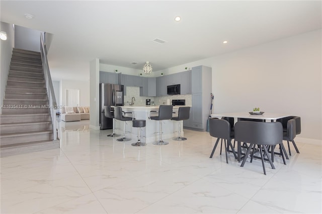 kitchen with marble finish floor, a breakfast bar, stainless steel fridge with ice dispenser, and gray cabinetry