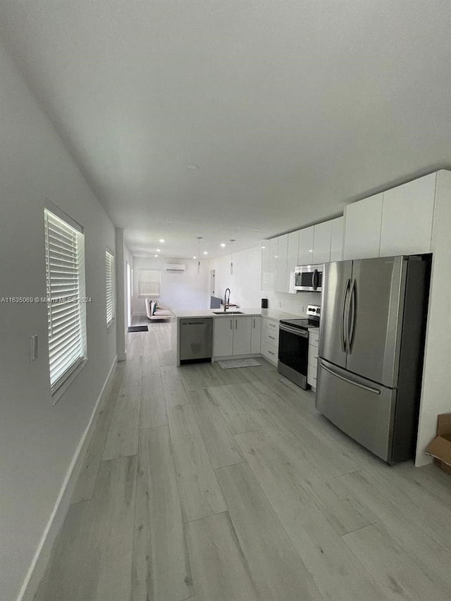 kitchen with light wood-type flooring, decorative light fixtures, stainless steel appliances, white cabinetry, and sink