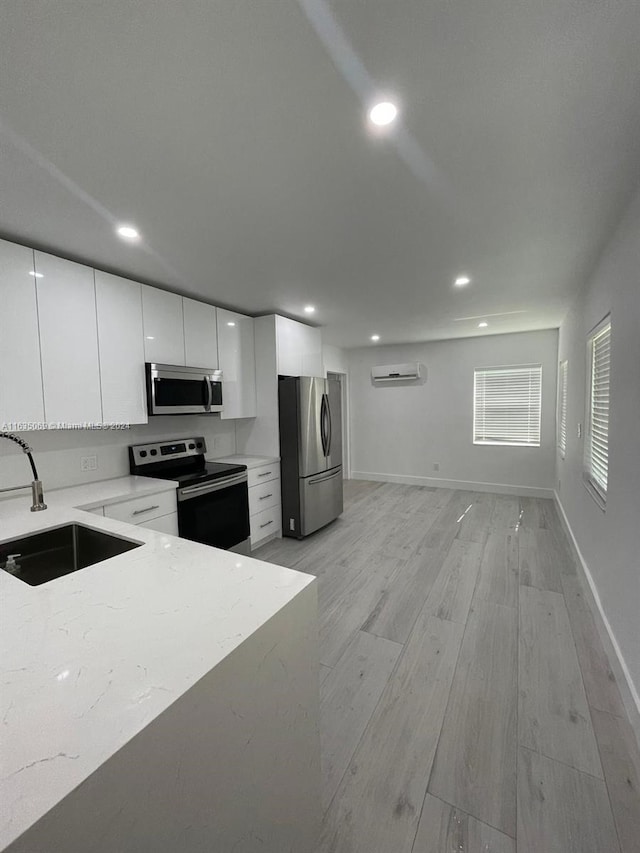 kitchen with light hardwood / wood-style flooring, a wall mounted air conditioner, stainless steel appliances, sink, and white cabinetry