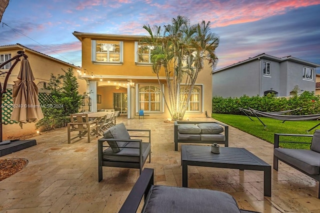 back house at dusk featuring an outdoor hangout area, a lawn, and a patio