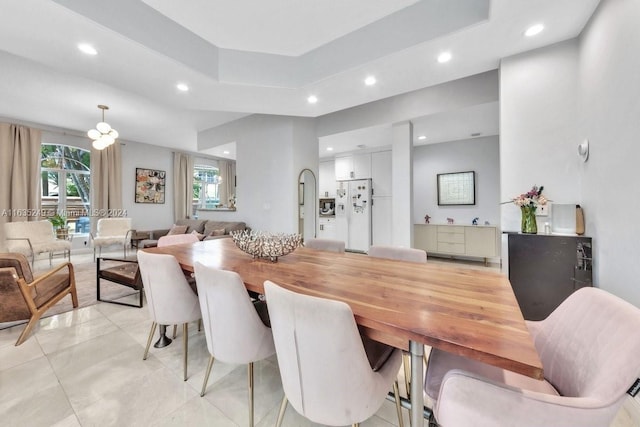 tiled dining area with a raised ceiling and a notable chandelier