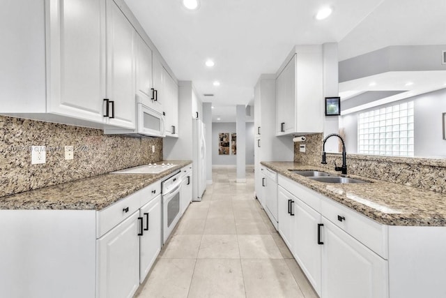 kitchen with white appliances, backsplash, light stone counters, sink, and white cabinets