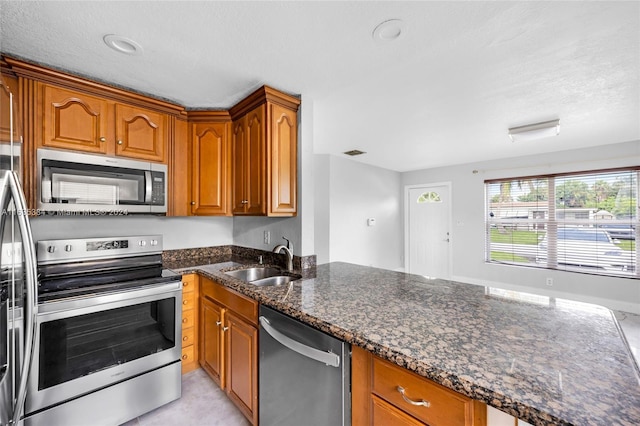 kitchen featuring dark stone countertops, a textured ceiling, appliances with stainless steel finishes, and sink