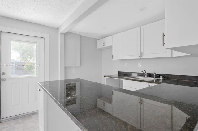 kitchen with dark stone countertops, white cabinets, and sink