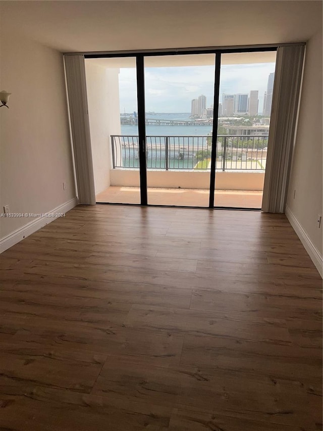 unfurnished room featuring floor to ceiling windows, hardwood / wood-style flooring, and a water view