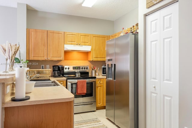 kitchen featuring light tile patterned floors, a textured ceiling, appliances with stainless steel finishes, light brown cabinetry, and sink