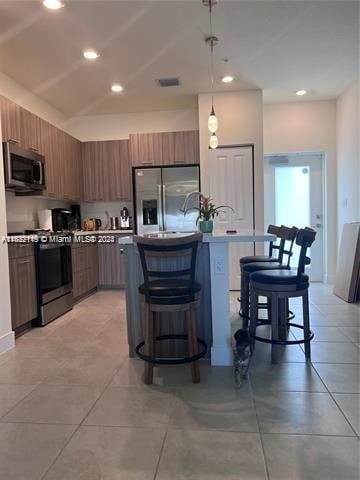 kitchen with light tile patterned flooring, stainless steel appliances, hanging light fixtures, and an island with sink