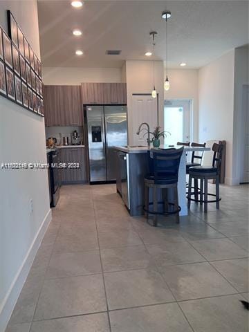 kitchen featuring light tile patterned flooring, stainless steel appliances, a center island with sink, and decorative light fixtures