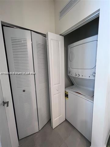 washroom with stacked washing maching and dryer and tile patterned flooring