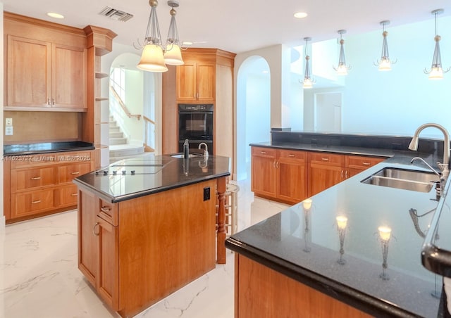 kitchen with double oven, a kitchen island with sink, sink, and hanging light fixtures