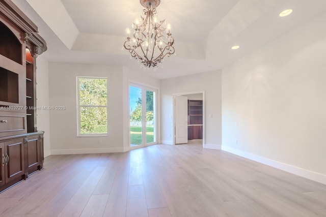 empty room featuring a chandelier, light wood-type flooring, and a tray ceiling