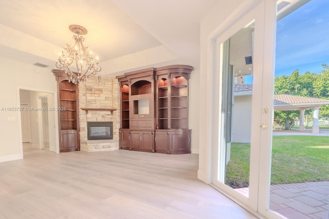 unfurnished living room featuring light hardwood / wood-style floors, built in features, a stone fireplace, and a notable chandelier