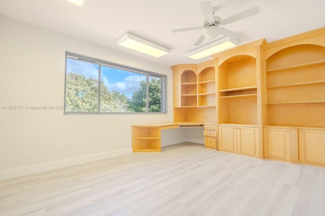 unfurnished office with light wood-type flooring, built in desk, and ceiling fan