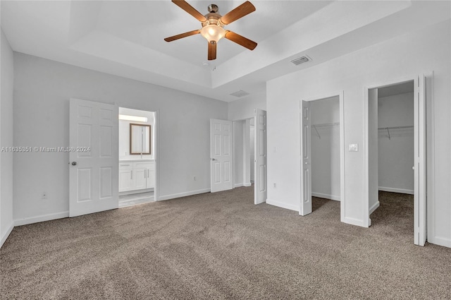 unfurnished bedroom featuring a spacious closet, ensuite bath, carpet flooring, ceiling fan, and a raised ceiling