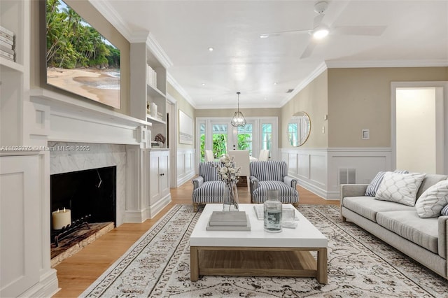 living room with built in shelves, ceiling fan, french doors, light hardwood / wood-style floors, and ornamental molding