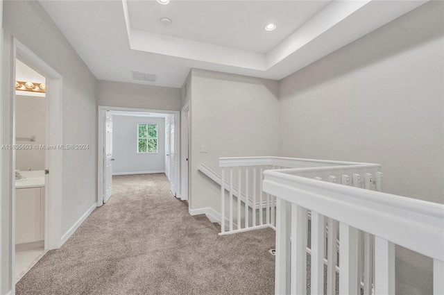 hallway with light carpet and a raised ceiling