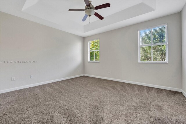 carpeted empty room with ceiling fan, a tray ceiling, and a wealth of natural light