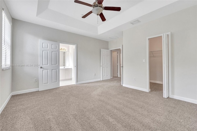 unfurnished bedroom featuring light carpet, ceiling fan, a raised ceiling, and a walk in closet