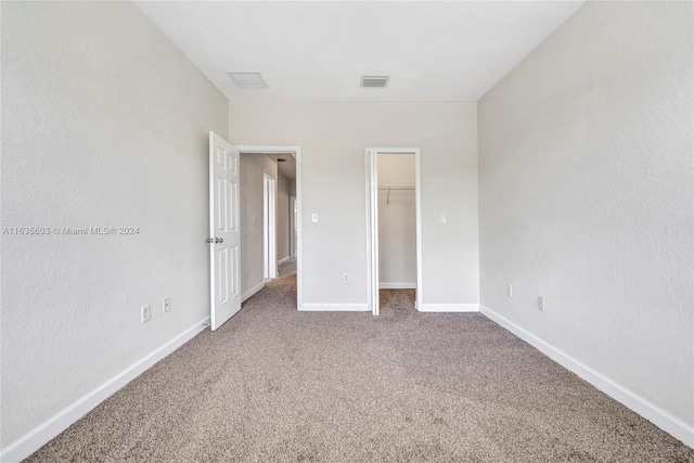 unfurnished bedroom featuring carpet, a walk in closet, and a closet