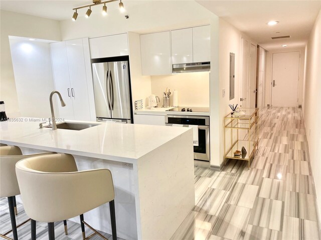 kitchen with track lighting, stainless steel appliances, white cabinets, sink, and a kitchen breakfast bar