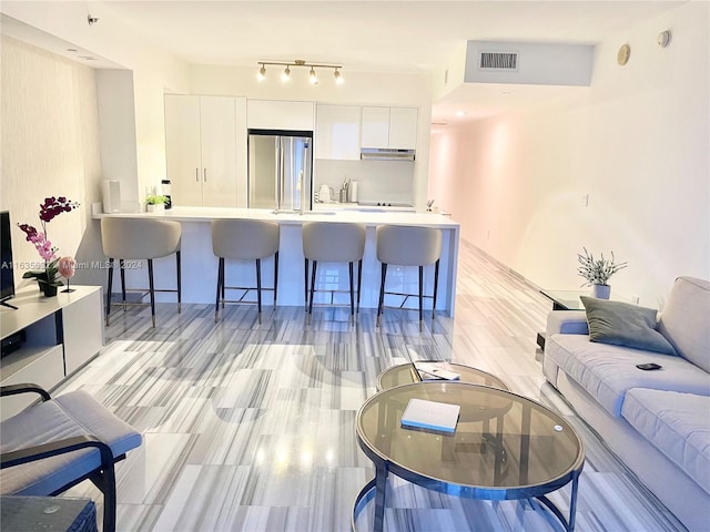 kitchen with white cabinetry, a breakfast bar, rail lighting, kitchen peninsula, and stainless steel fridge