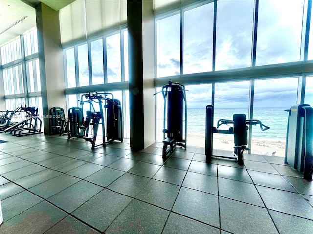 workout area with expansive windows, a water view, tile patterned flooring, and a towering ceiling