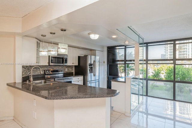 kitchen featuring tasteful backsplash, hanging light fixtures, appliances with stainless steel finishes, kitchen peninsula, and white cabinets