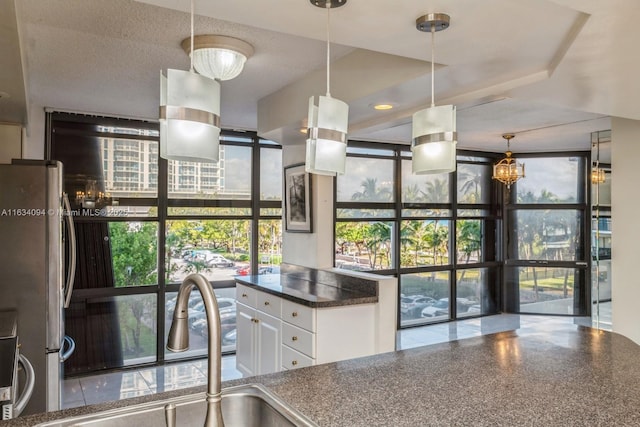 kitchen featuring dark countertops, expansive windows, freestanding refrigerator, white cabinetry, and a sink