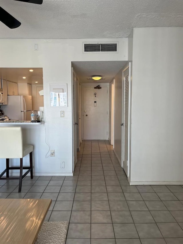 hall featuring light tile patterned floors, baseboards, visible vents, and a textured ceiling