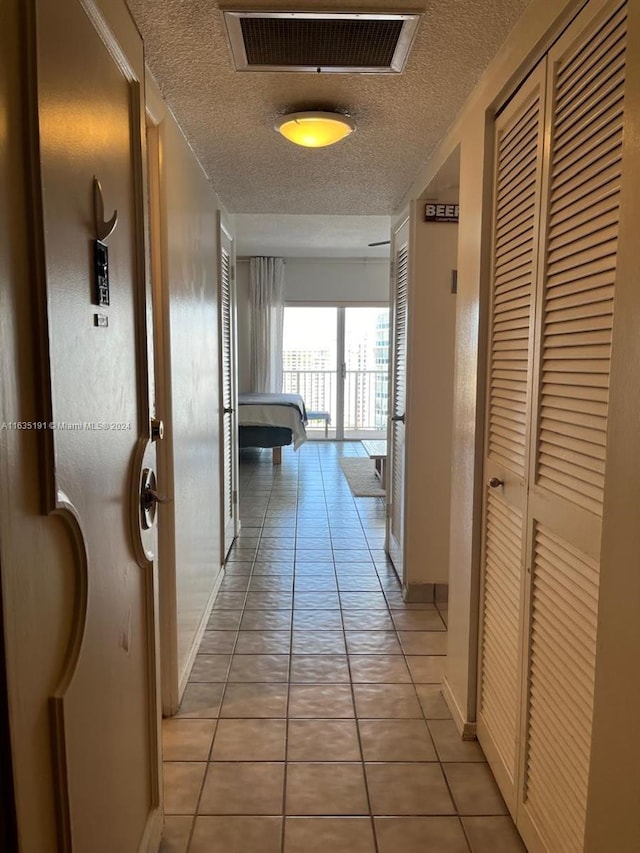 hall with visible vents, a textured ceiling, baseboards, and light tile patterned floors