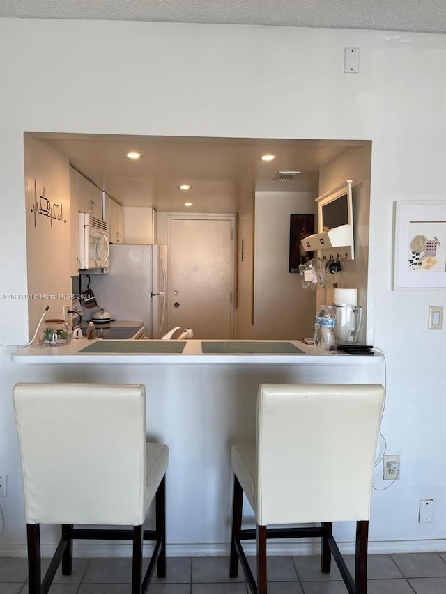 kitchen with a breakfast bar area, recessed lighting, visible vents, white appliances, and tile patterned floors