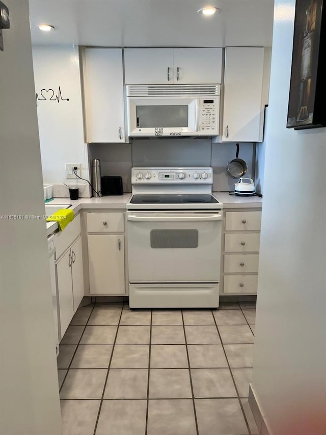 kitchen with light tile patterned floors, light countertops, white appliances, and white cabinets