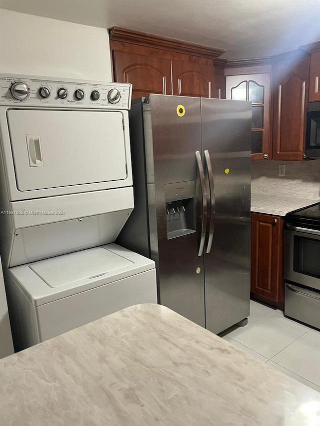 kitchen with light tile patterned floors, stainless steel appliances, stacked washer / drying machine, and tasteful backsplash