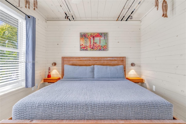 bedroom featuring rail lighting and wood walls