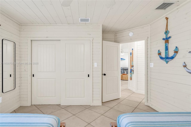 bedroom with light tile patterned floors, wooden ceiling, wooden walls, visible vents, and a closet