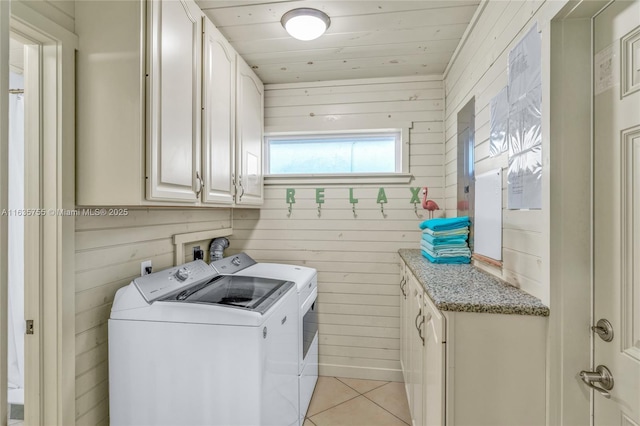 clothes washing area with light tile patterned floors, wooden ceiling, washing machine and dryer, wooden walls, and cabinet space