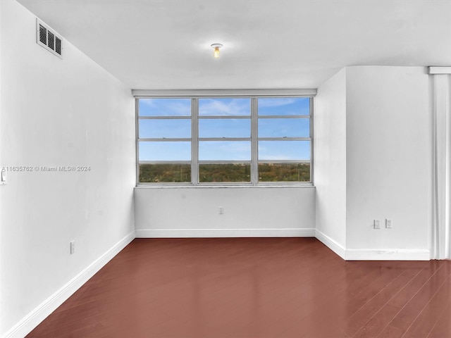 empty room with dark wood-style floors, baseboards, visible vents, and a wealth of natural light