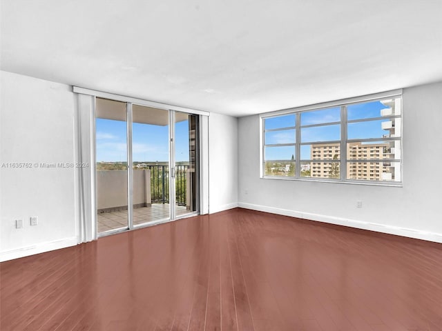 empty room with floor to ceiling windows, baseboards, and wood finished floors