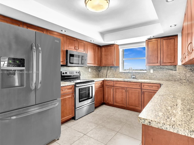 kitchen featuring appliances with stainless steel finishes, a tray ceiling, a sink, and backsplash