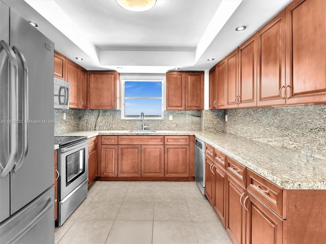 kitchen featuring appliances with stainless steel finishes, a raised ceiling, brown cabinetry, and a sink