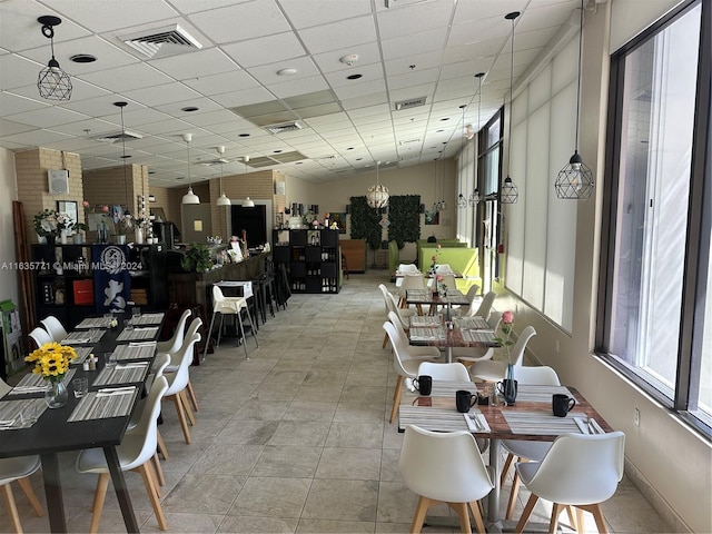 dining room with a drop ceiling, light tile patterned floors, and brick wall