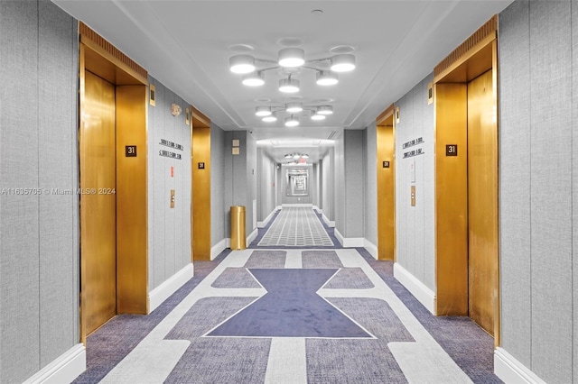 hall featuring elevator, a notable chandelier, and carpet flooring