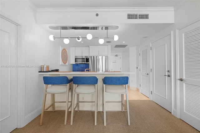 kitchen with white cabinetry, stainless steel appliances, crown molding, light carpet, and a breakfast bar