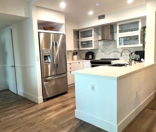 kitchen with a sink, light countertops, wall chimney range hood, dark wood-style floors, and stainless steel fridge