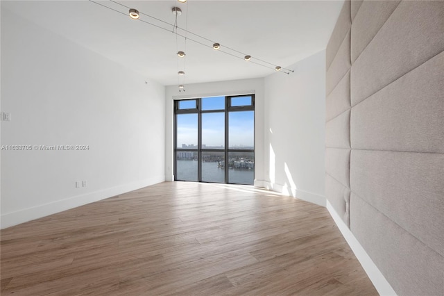 unfurnished room featuring a water view, baseboards, and wood finished floors