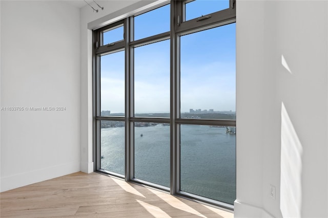 spare room with a water view, light wood-style flooring, and baseboards