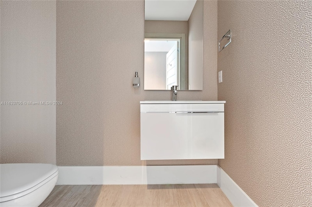 half bath featuring a textured wall, vanity, toilet, and wood finished floors