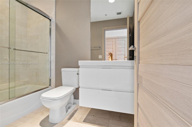 bathroom with toilet, bath / shower combo with glass door, visible vents, vanity, and tile patterned floors