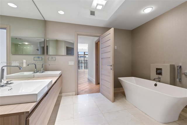 full bathroom featuring double vanity, visible vents, tile patterned flooring, a freestanding bath, and a sink