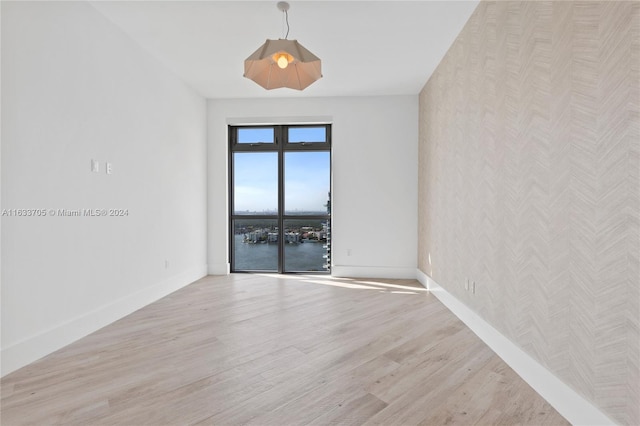 spare room with a water view, light wood-style flooring, and baseboards